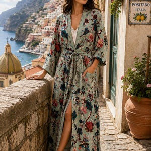 May include: A floor-length, light green robe featuring a vibrant floral pattern in shades of red, blue, and dark brown. The garment includes long, wide sleeves, a matching tie belt at the waist, and two front pockets, worn over a white camisole.