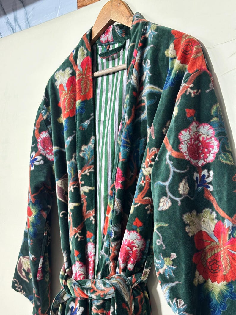 May include: A dark green velvet robe featuring a vibrant floral pattern with red, pink, and blue blossoms on winding branches. The garment includes a matching tie belt and a contrasting interior lining with thin vertical white and green stripes.