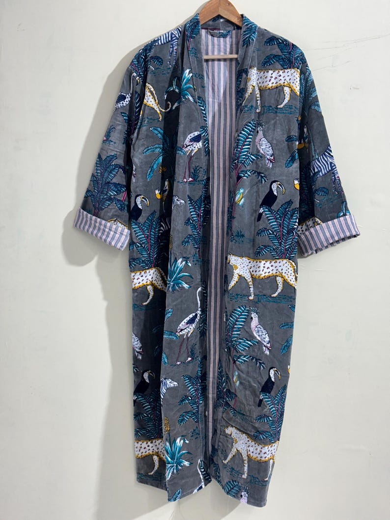 May include: A long-sleeved robe in a dark gray hue featuring a repeating pattern of leopards, toucans, and tropical foliage in white, yellow, and blue. The garment has an open front design with a vertical striped lining visible along the inner edges.
