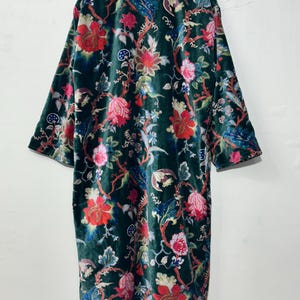 May include: A long-sleeved velvet robe in a deep forest green color, featuring a vibrant floral pattern with large red, pink, and blue blossoms, winding stems, and intricate foliage. The garment has a straight silhouette and a high collar.