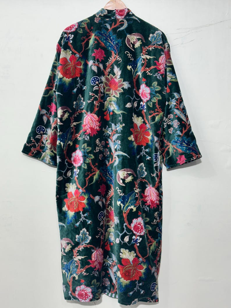 May include: A long-sleeved velvet robe in a deep forest green color, featuring a vibrant floral pattern with large red, pink, and blue blossoms, winding stems, and intricate foliage. The garment has a straight silhouette and a high collar.