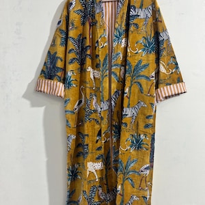May include: A long-sleeved mustard yellow robe featuring an all-over print of zebras, leopards, and tropical palm trees. The garment has an open front design with white and orange vertical striped cuffs and an interior lining in the same pattern.