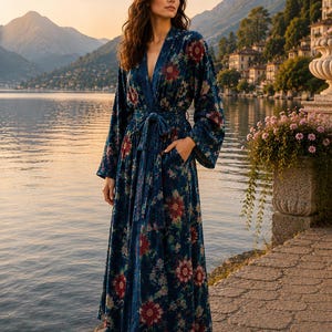 May include: A floor-length, long-sleeved robe in a deep blue velvet fabric featuring a repeating floral pattern in shades of red, pink, and green. The garment includes a matching tie belt at the waist, a V-neckline, and two side pockets.
