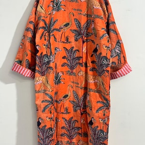 May include: An orange long-sleeve robe featuring a repeating print of leopards, flamingos, toucans, and zebras among palm trees. The garment has a mandarin collar and cuffs with a red and white vertical striped pattern on the interior lining.