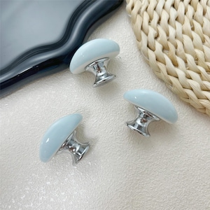 Peut inclure: Trois boutons de meuble en forme de champignon bleu clair avec des bases argentées brillantes. Les boutons sont disposés sur une surface claire, avec un objet gris foncé et un tapis de paille tressée en arrière-plan. Boutons décoratifs.