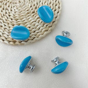 May include: Four turquoise cabinet knobs with silver-colored bases are displayed on a light background. Two knobs are loose, while the other two are attached. The knobs have a smooth, rounded shape, and the turquoise color is vibrant.