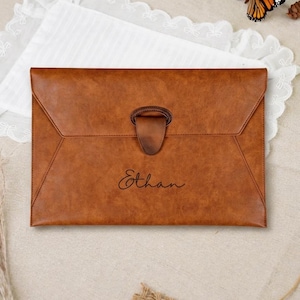 May include: A rectangular brown document folder with a flap closure and a central loop fastener. The front surface features the name Ethan engraved in a cursive script. The folder has a smooth, uniform texture and a structured envelope design.