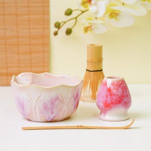 Puede incluir: Un juego de té matcha con un cuenco de cerámica rosa con diseño de loto, un batidor de bambú, un soporte para batidor de cerámica rojo y rosa y una cuchara de bambú. Para preparar té matcha.