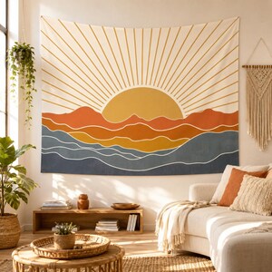 Puede incluir: Un tapiz de pared rectangular que presenta una ilustración gráfica de un sol saliendo sobre cadenas montañosas superpuestas. El diseño utiliza una paleta de amarillo mostaza, naranja quemado y azul oscuro, con líneas blancas finas.