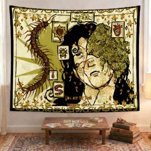 May include: A square wall tapestry featuring a stylized illustration of a face partially covered in green foliage, a large brown centipede, and small framed icons of a flower, beetle, heart, and worm. The text reads, You are the flesh maggots adore.