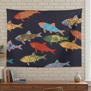 May include: A dark blue tapestry featuring a school of colorful fish. The fish are in various colors, including orange, yellow, green, and blue, with patterned designs. The tapestry is hanging on a white brick wall.