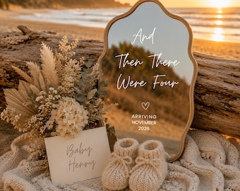 May include: A scalloped-edge mirror with the white text And Then There Were Four, a heart icon, and ARRIVING NOVEMBER 2026. Beside it sits a bouquet of dried flowers, a card reading Baby Henry, and a pair of beige knit baby booties on a cream blanket.