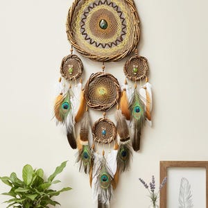 May include: A handcrafted dreamcatcher with a woven rattan frame and intricate web design. It features peacock feathers, beads, and smaller dreamcatchers hanging below. The color palette includes natural tones, brown, and teal.