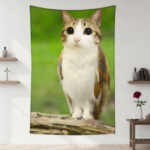 Op de afbeelding: Een wandtapijt met een grillig ontwerp van een kat met uilachtige kenmerken. De kat heeft grote, expressieve ogen, bruine en witte vacht en uilachtige vleugels. De achtergrond is een levendig groen, wat een opvallend contrast creëert.