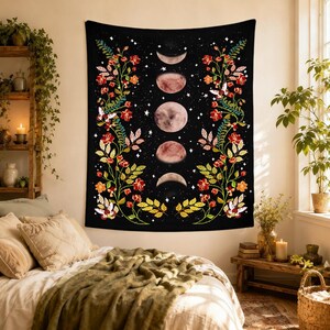 May include: A black rectangular wall tapestry featuring a vertical sequence of five moon phases in the center, surrounded by two symmetrical floral vines with red, orange, and yellow flowers and green leaves against a starry night sky background.