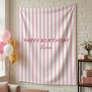 May include: A pink and white striped backdrop with the text "HAPPY BIRTHDAY Luna" in pink lettering. Balloons in pink, white, and gold are in the foreground. The backdrop is hanging on a white brick wall.
