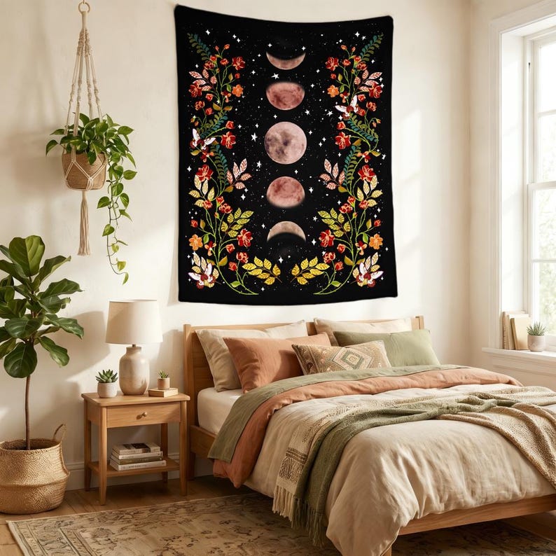 May include: A rectangular wall tapestry featuring a black background with a vertical central column of five moon phases in varying shades of pink and white, flanked by two symmetrical floral vines with red, orange, and yellow flowers and green leaves.