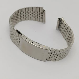 Könnte beinhalten: Ein silberfarbenes Metall-Uhrenarmband mit einem netzartigen Design. Das Armband ist unbefestigt und zeigt die Schließe und die Enden, die mit einem Zifferblatt verbunden werden. Das Wort "CASIO" ist auf der Schließe zu sehen.