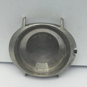 May include: A silver-coloured watch case with two lugs at the top and a crown on the side. The inside of the case has the text "FORTIS WATCH LTD" and other markings. The case is round and appears to be made of metal.