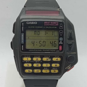 May include: A vintage Casio Wrist Remote Controller watch. The black watch features a calculator keypad, a digital display showing the time, and control buttons. The watch has the text "CASIO" and "WRIST REMOTE CONTROLLER" printed on the face.