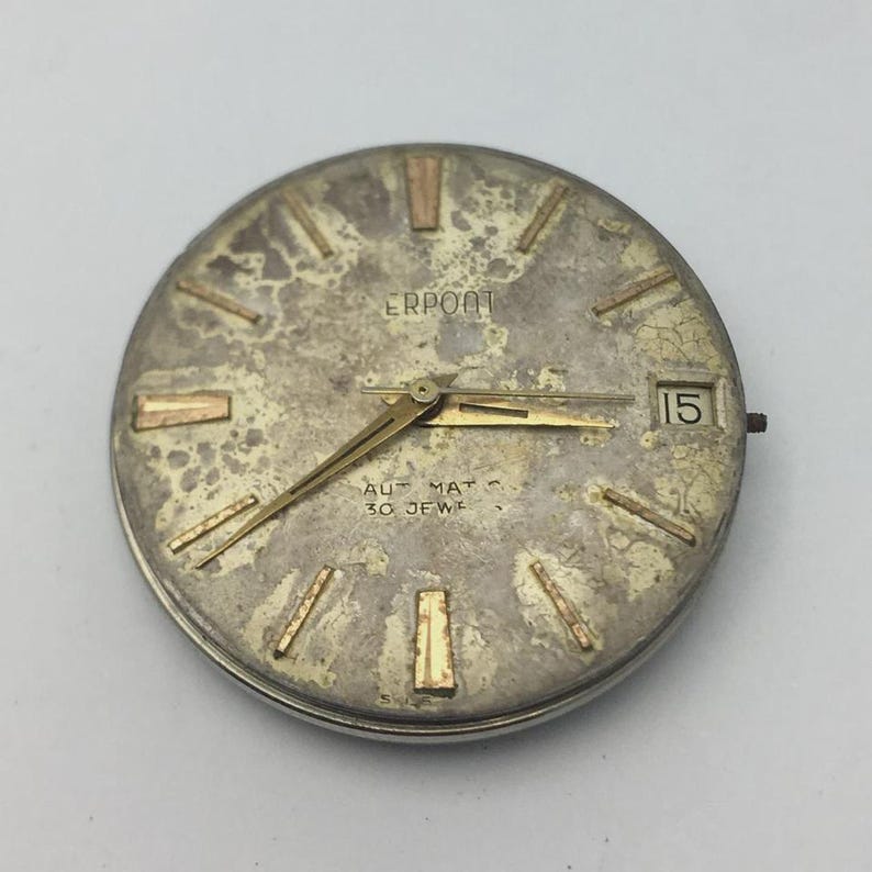 K&ouml;nnte beinhalten: Ein Vintage-Zifferblatt in Silber- und Goldt&ouml;nen. Das Zifferblatt hat ein verwittertes Aussehen mit goldfarbenen Stundenmarkierungen und Zeigern. Das Datum wird als "15" angezeigt. Der Markenname "ERPOOT" ist sichtbar.