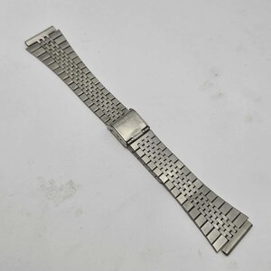 May include: A silver-colored watch band with a woven metal design. The band features a clasp and is designed to attach to a watch face. The band is made of a shiny, metallic material.