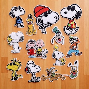 May include: A collection of embroidered patches featuring various characters from the Peanuts comic strip. The patches showcase Snoopy in different outfits, along with other characters like Charlie Brown, Lucy, and Woodstock. The patches are outlined in black and have a white background.