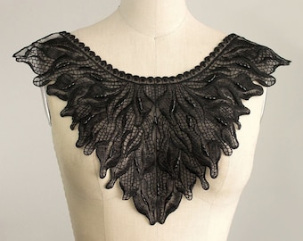 May include: Black lace collar with a scalloped edge and a delicate floral design. The collar is made of a sheer fabric and has a beaded embellishment.