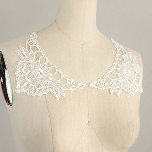 May include: White lace collar trim with a floral design. The trim is made of delicate lace and features a scalloped edge.