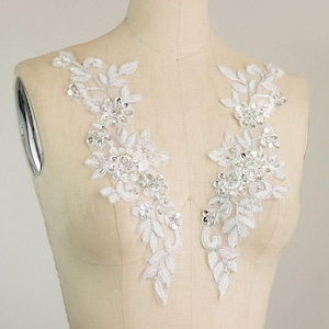 May include: Two white lace appliques with silver sequins and beads, perfect for adding a touch of elegance to a wedding dress or other garment.