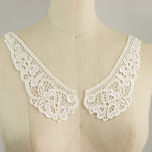 May include: White lace collar with a delicate floral pattern. The collar is made of a soft, lightweight fabric and has a scalloped edge.