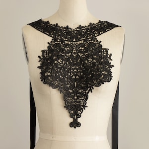 May include: Black lace collar with a delicate floral pattern. The collar is designed to be worn around the neck and shoulders.