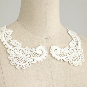 May include: White lace collar with a delicate floral pattern. The collar is made of a soft, lightweight fabric and is perfect for adding a touch of elegance to any outfit.
