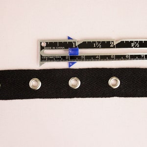 Pu&ograve; includere: Nastrino in cotone nero con quattro occhielli argentati. Il nastro &egrave; largo 2,5 cm e viene misurato con un righello.