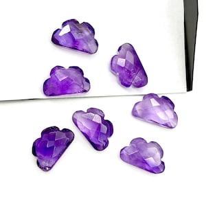 May include: A selection of cloud-shaped amethyst gemstones. The gemstones are a vibrant purple hue and feature a faceted cut, giving them a sparkling appearance. They are presented on a white surface.