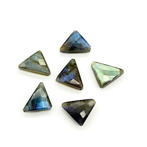 May include: Six triangular labradorite gemstones with faceted surfaces are arranged on a white background. The stones display a range of colors, including blues, greens, and grays, with iridescent flashes. The gemstones are likely for jewelry making.