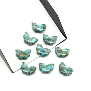 May include: Nine turquoise butterfly-shaped gemstone beads with gold veining. The beads are arranged on a white surface with a black accent. These decorative beads are ideal for jewelry making and crafts.