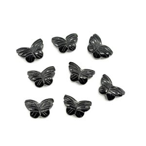 May include: A collection of eight black butterfly-shaped beads. Each bead features detailed wing patterns and a smooth, polished finish. The beads are scattered on a white surface, showcasing their intricate design.