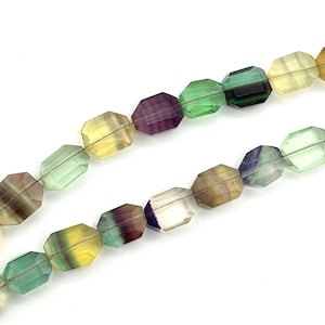 Può includere: Due fili di perline sfaccettate di fluorite multicolore. Le perline sono rettangolari con angoli arrotondati, che mostrano una gamma di colori tra cui verde, viola, giallo e marrone. Le perline sono infilate, pronte per la creazione di gioielli.