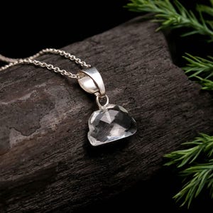 Peut inclure: Un pendentif en pierre précieuse transparente et facettée en forme de nuage, suspendu à une fine chaîne en argent. Le pendentif comporte une bélière métallique polie qui relie la pierre à la délicate chaîne à maillons, offrant une surface brillante.