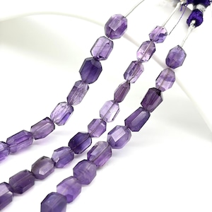 May include: Three strands of faceted amethyst beads. The beads are a deep purple color and are strung on a silver wire. The beads are rectangular with cut edges. The background is white.