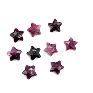Op de afbeelding: Een verzameling facetgeslepen, stervormige edelstenen in verschillende tinten paars en donkerrood. De edelstenen zijn verspreid op een witte achtergrond, waarbij hun geometrische sneden en natuurlijke kleurvariaties worden getoond. Ideaal voor sieraden of knutselen.