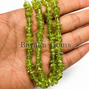 Può includere: Una collana composta da piccole scaglie di peridoto verde lime, traslucide e di forma irregolare. Le pietre sono infilate in una linea continua, mostrando un colore vivace e naturale. Il testo Baraka Gems è visibile.