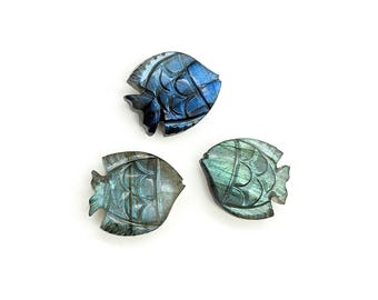 Puede incluir: Tres figuras de peces talladas en labradorita. Los peces tienen patrones detallados y diferentes tonos de azul y verde. Las figuras se muestran sobre un fondo blanco.
