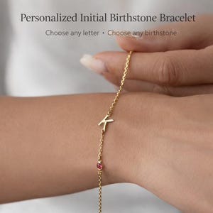 May include: A gold-colored bracelet with the letter "K" and a small pink gemstone. The bracelet is on a wrist. The text at the top says "Personalized Initial Birthstone Bracelet". Below the text it says "Choose any letter • Choose any birthstone".