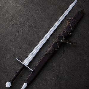 Peut inclure: Une épée en acier à double tranchant avec une garde droite, une poignée noire et un pommeau rond. À côté de l'épée se trouve un fourreau en cuir marron foncé doté d'une bouterolle en métal et d'un système complexe de lanières en cuir.