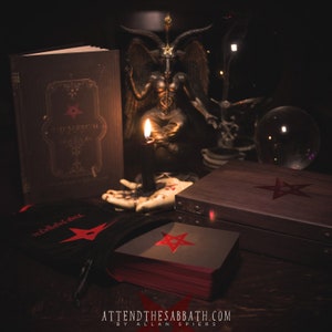 Könnte beinhalten: Ein Tarot-Set bestehend aus einem schwarzen Buch mit dem Titel The Sabbath, einer Baphomet-Statue, einer schwarzen Kerze in einem handförmigen Halter, einer Holzbox mit rotem Pentagramm und einem schwarzen Samtbeutel mit rotem Pentagramm.