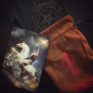 Pu&ograve; includere: Una carta dei tarocchi con un bordo dorato e una rappresentazione di un uomo nudo che cavalca un cavallo bianco. La carta fa parte di un mazzo di tarocchi con un pentagramma e rune sul retro delle carte. Le carte sono in una borsa di velluto marrone con un pentagramma rosso.