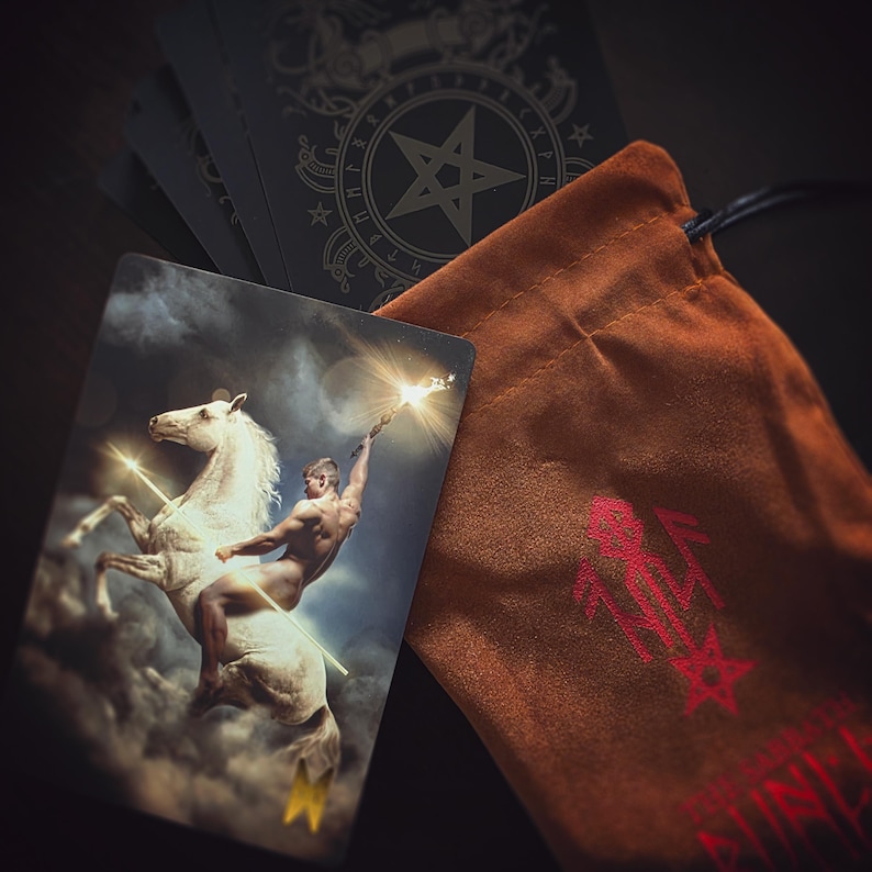 Pu&ograve; includere: Una carta dei tarocchi con un bordo dorato e una rappresentazione di un uomo nudo che cavalca un cavallo bianco. La carta fa parte di un mazzo di tarocchi con un pentagramma e rune sul retro delle carte. Le carte sono in una borsa di velluto marrone con un pentagramma rosso.