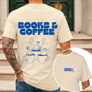 Könnte beinhalten: Cremefarbenes T-Shirt mit dem blauen Text "BOOKS & COFFEE" auf dem Rücken und einer kleinen Version auf der Vorderseite. Die Grafik auf der Rückseite zeigt Personen, die in Kaffeetassen entspannen und lesen. Ein lässiges T-Shirt für Bücher- und Kaffeeliebhaber.